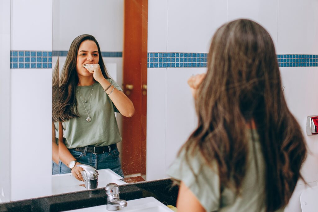 A young woman brushes her teeth, looking in the bathroom mirror. Self-care and hygiene concept.
